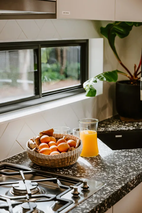 A kitchen counter with a bowl of oranges beside a glass of juice.