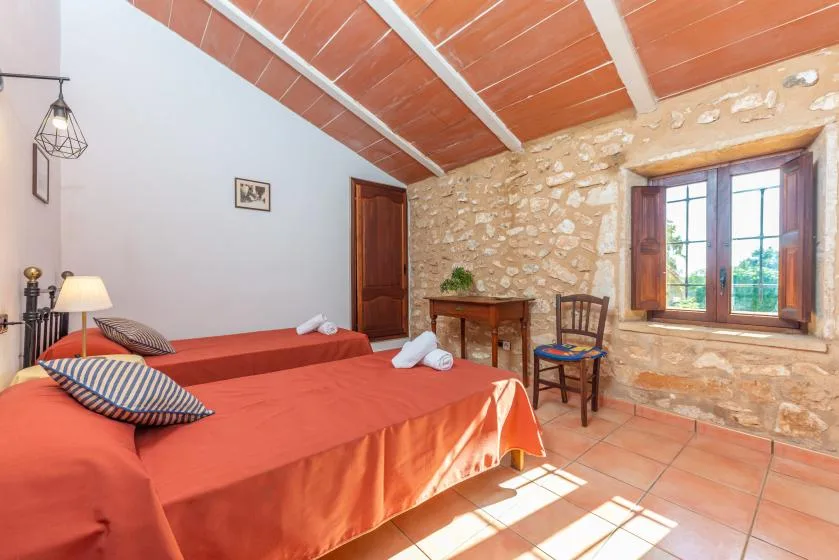 Un dormitorio con dos camas junto a una pared de piedra y una ventana iluminada por el sol.