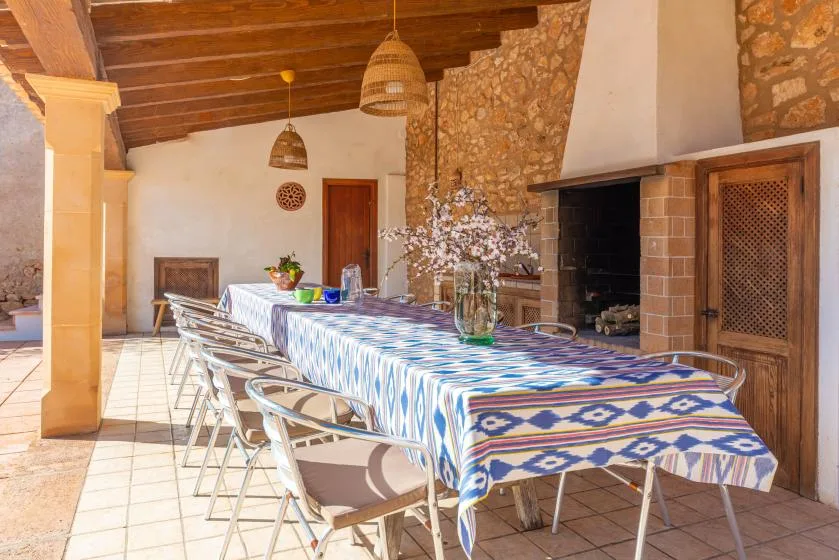 Comedor exterior cubierto con una mesa larga bajo un techo de madera.