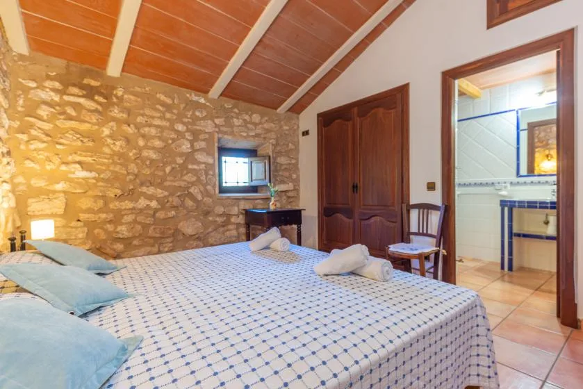 Un dormitorio con una cama grande, una pared de piedra y techo de madera.