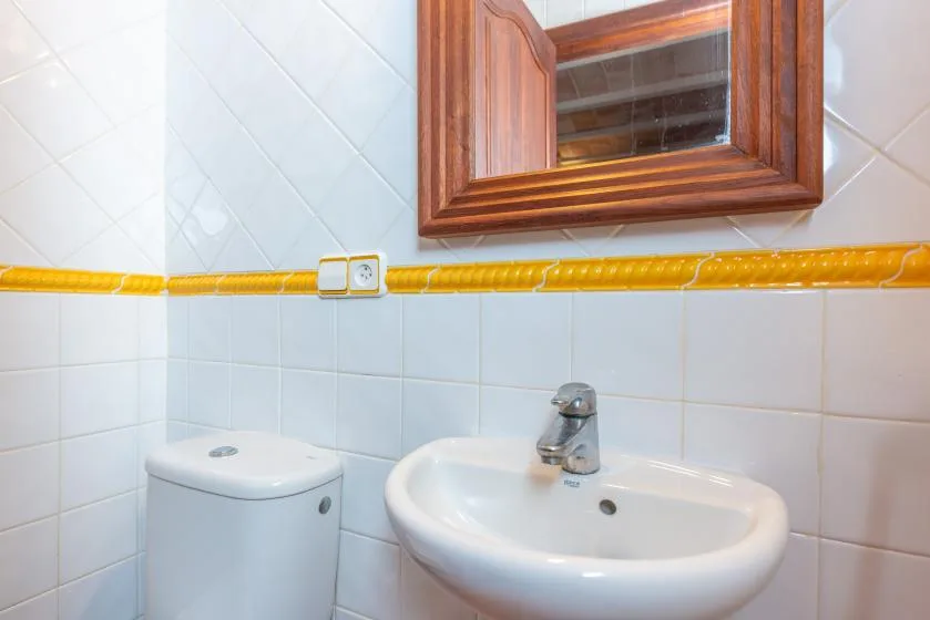 Un baño alicatado con lavabo, inodoro y espejo con marco de madera.