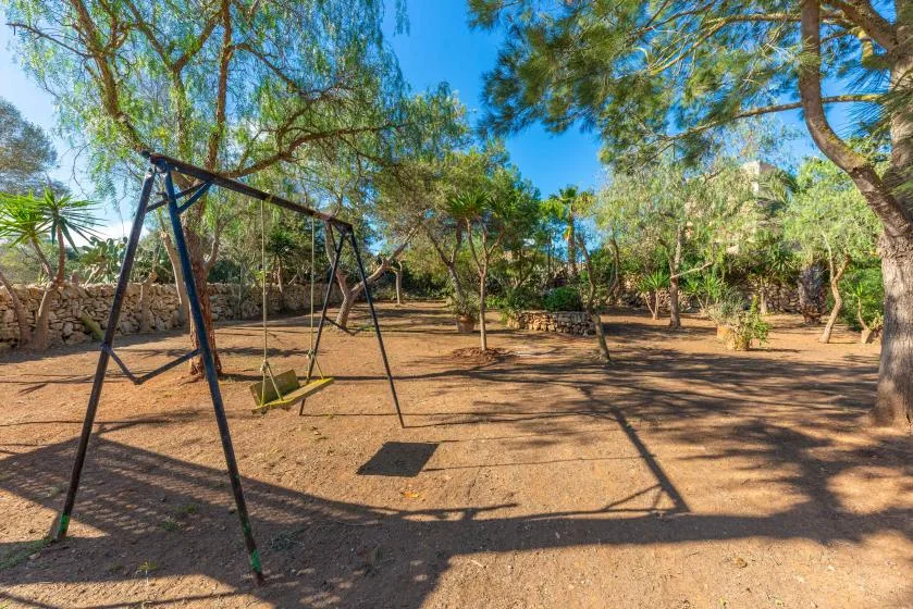Un columpio está en una zona de juegos al aire libre, entre árboles.