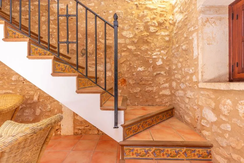 Una escalera de baldosas con barandilla metálica oscura junto a paredes de piedra vista.