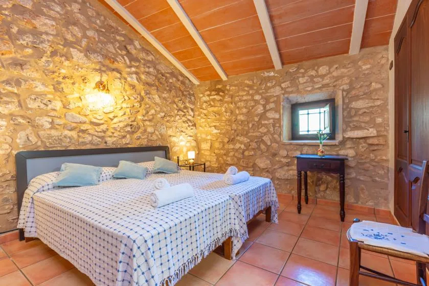 Un dormitorio con una cama doble, paredes de piedra y una ventana pequeña.