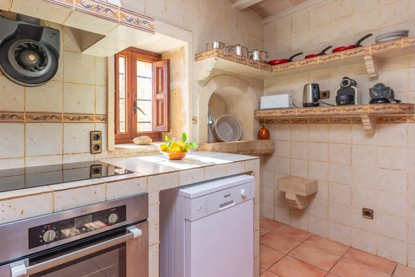 Una cocina con azulejos, encimera, horno, lavavajillas y estantes abiertos.