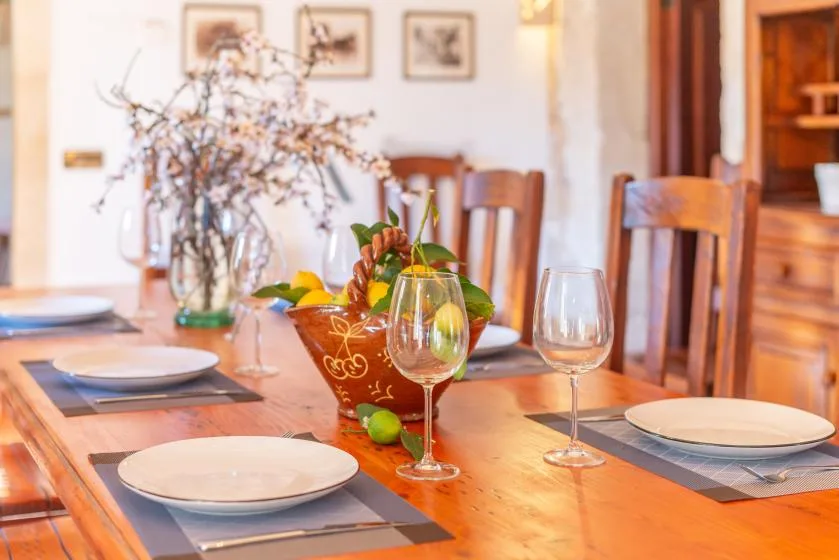 Una mesa de comedor está puesta con platos, copas y un cuenco de fruta.