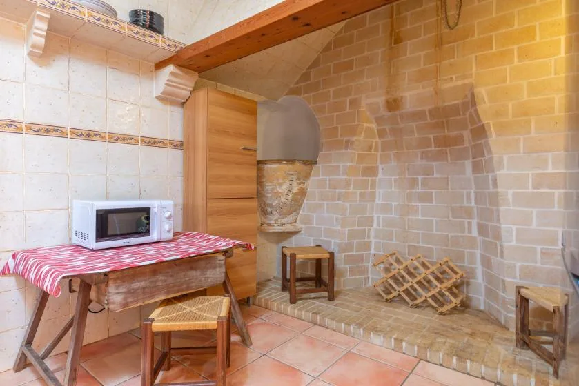 Una habitación alicatada con un microondas sobre una mesa y un pequeño taburete de madera.