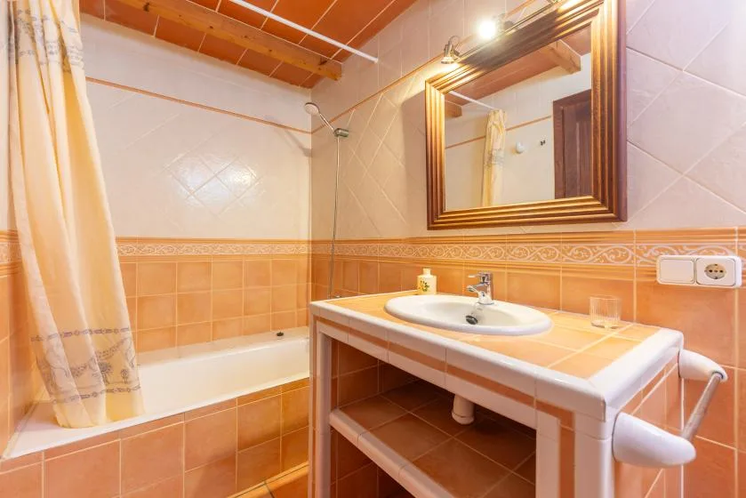 Un baño alicatado con bañera, cortina de ducha y lavabo bajo un espejo.