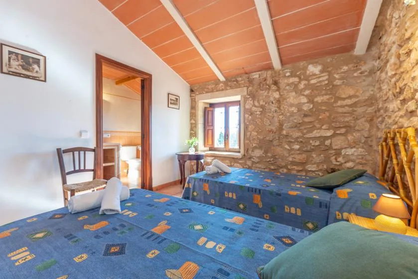 Un dormitorio rústico con camas cubiertas de azul, paredes de piedra y una ventana pequeña.