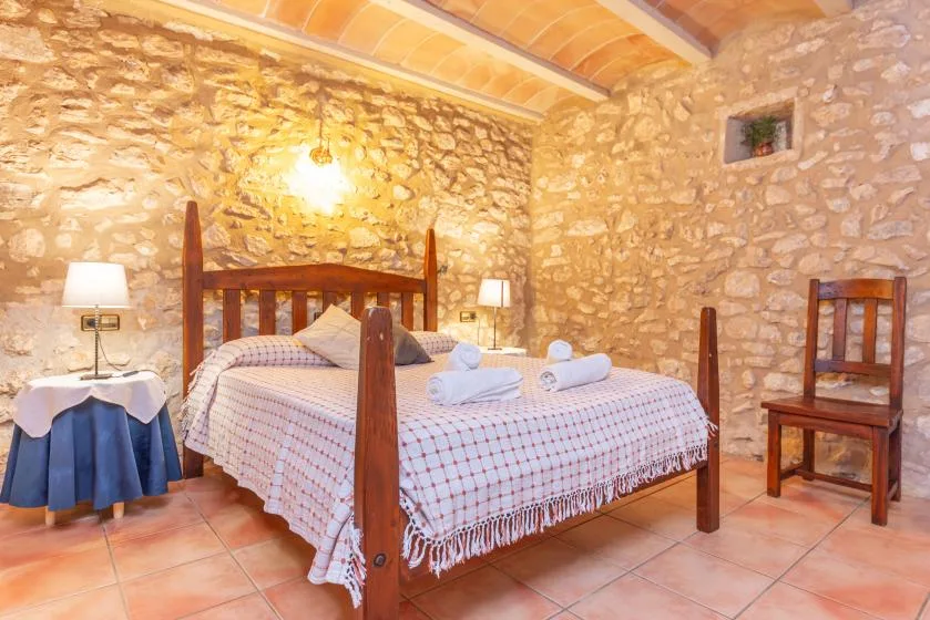 Un dormitorio con una cama de madera, paredes de piedra y suelo de baldosas.