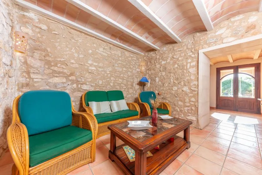 Una sala de estar con paredes de piedra, asientos verdes y una mesa de centro de madera.