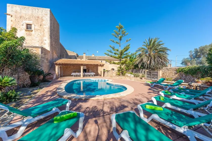 Una piscina y tumbonas ocupan un patio soleado al aire libre junto a un edificio de piedra.