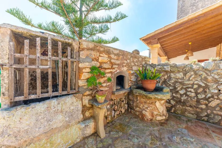 Un patio de piedra con un pequeño horno arqueado y plantas en macetas.