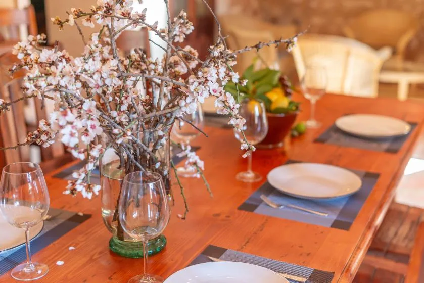 Una mesa de comedor está puesta con platos y ramas florales en un jarrón.