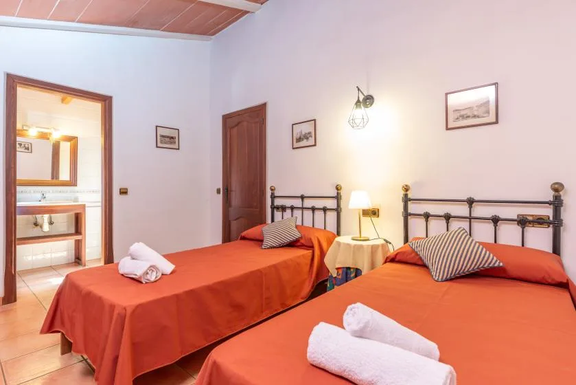Un dormitorio con dos camas vestidas con ropa de cama naranja y toallas dobladas.