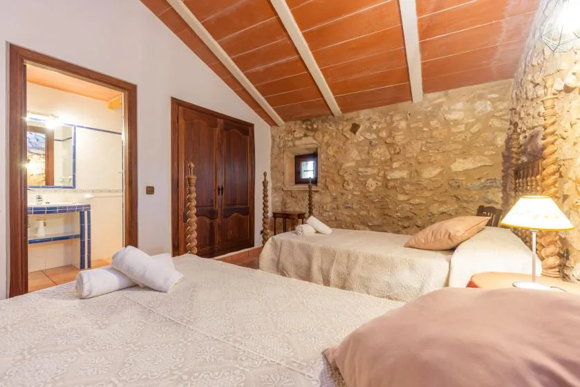 Un dormitorio con camas bajo un techo inclinado de madera y paredes de piedra.
