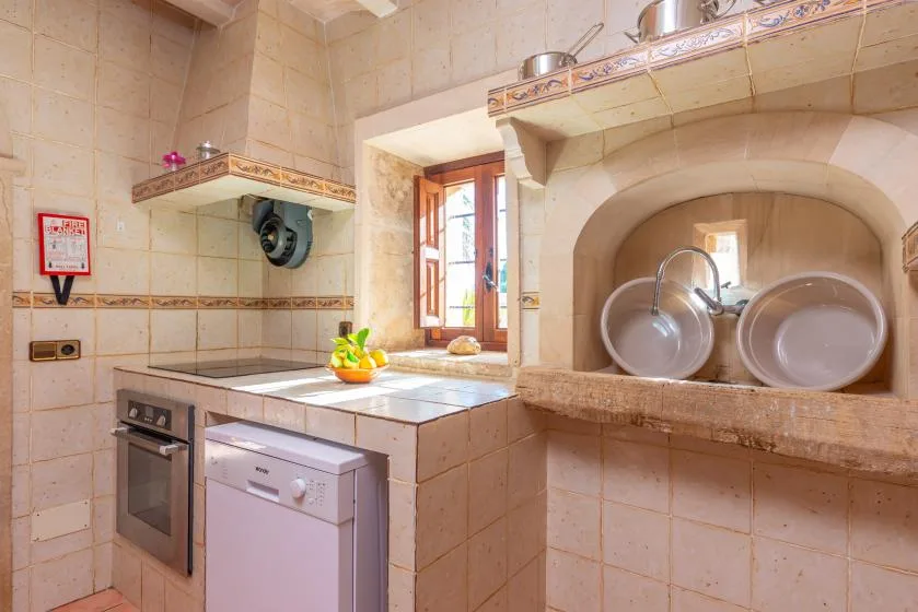 Una cocina alicatada con encimera, fregadero y platos en un nicho empotrado.