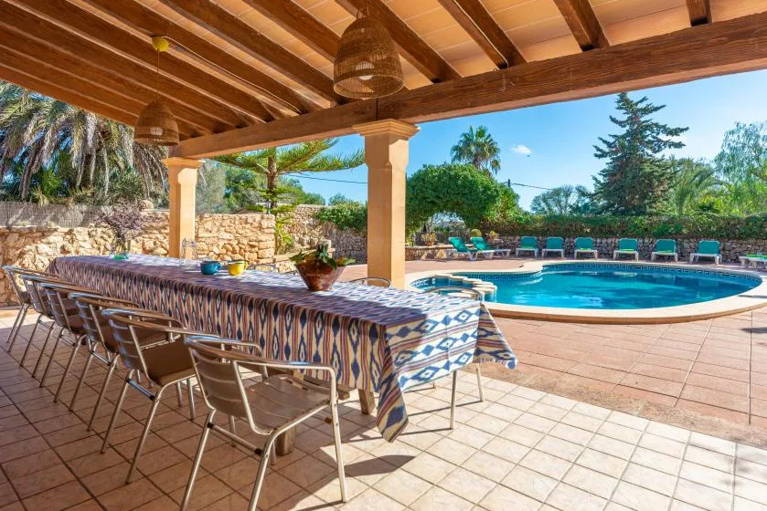 Una zona de comedor al aire libre cubierta da a una piscina y un jardín.
