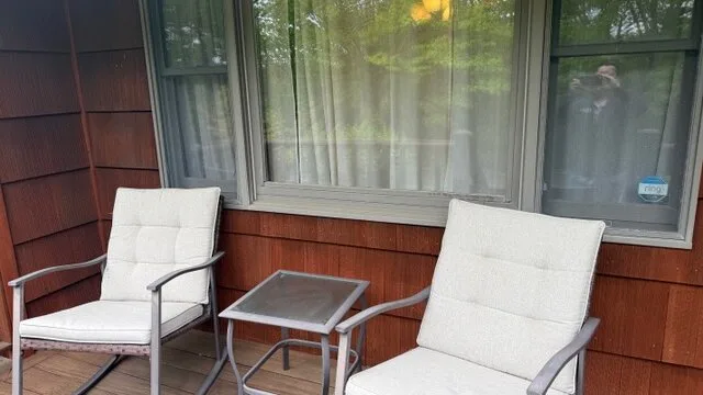 Una pequeña zona de estar al aire libre con dos asientos acolchados y una mesa junto a una ventana.