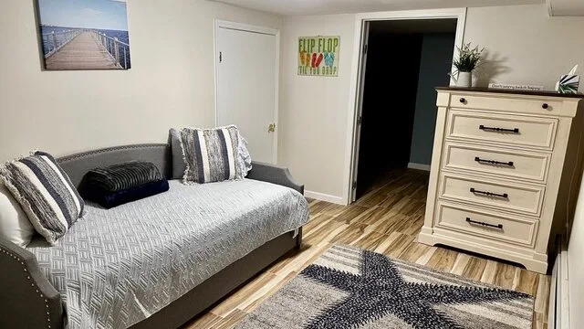 Un dormitorio con un sofá cama, una alfombra estampada y una cómoda.