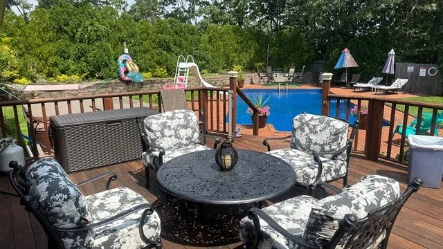 Una terraza de madera con asientos al aire libre da a una piscina.