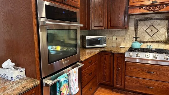 Una cocina con gabinetes de madera, hornos empotrados y una estufa.