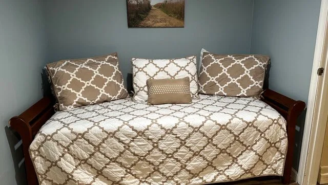 Un diván con ropa de cama estampada y cojines está junto a una pared azul claro.