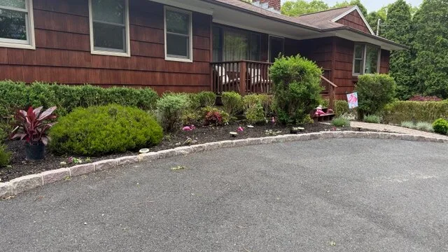 Un edificio de revestimiento rojo se encuentra detrás de un jardín y una entrada pavimentada.