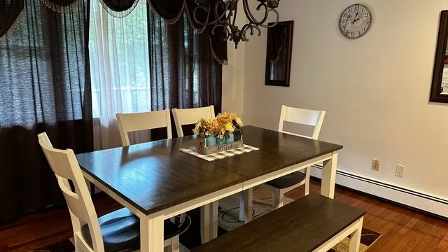 Un comedor con una mesa rectangular oscura y sillas bajo una lámpara colgante.