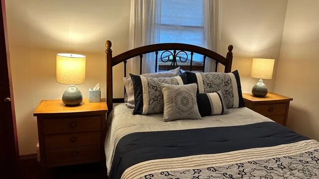 Un dormitorio con una cama adornada con cojines estampados y una manta oscura.