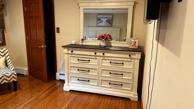 Una cómoda de dormitorio con espejo está junto a la pared, sobre un piso de madera.