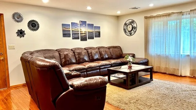 Una sala de estar con asientos marrones, una mesa de centro y grandes ventanas con cortinas.