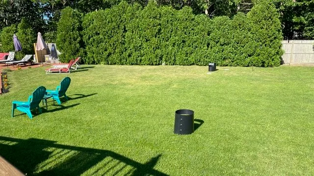Un césped al aire libre con asientos verdes y tumbonas junto al seto.