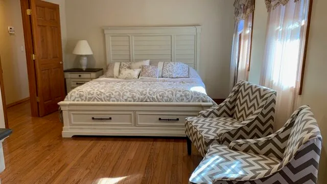 Un dormitorio con una cama, una mesita de noche y asientos estampados junto a la ventana.