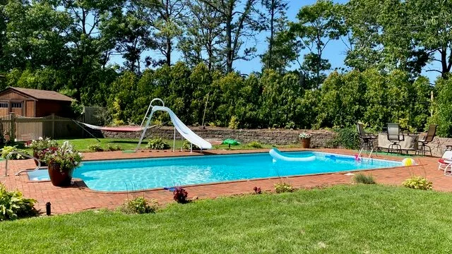 Una piscina al aire libre con un tobogán, patio y césped alrededor.
