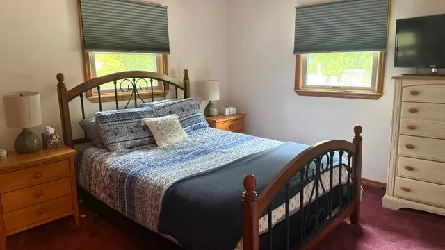 Un dormitorio con una cama vestida con ropa de cama azul y ventanas con persianas.