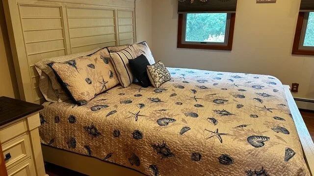 Un dormitorio con una cama cubierta con una colcha estampada y ventanas encima.