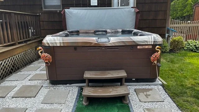 Una bañera de hidromasaje exterior está sobre un patio pavimentado junto a una terraza de madera.