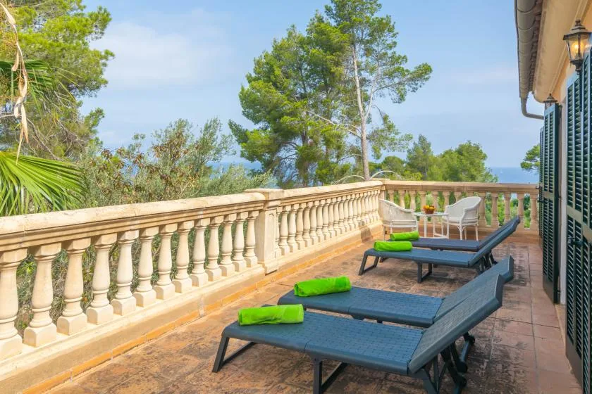 A tiled terrace with lounge seating overlooks a stone balustrade and leafy trees.