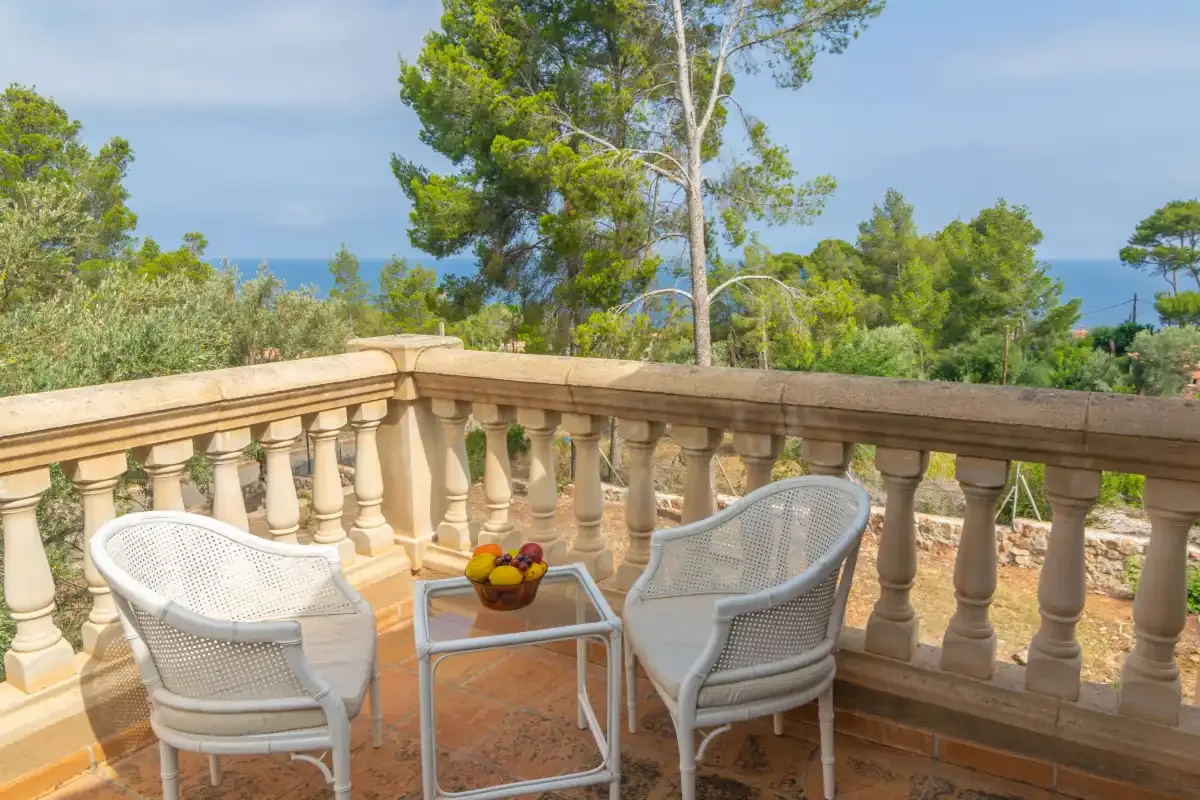 A tiled terrace with seating overlooks trees and the sea.