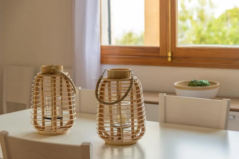 A dining table by a window holds two woven candle holders and a small bowl.