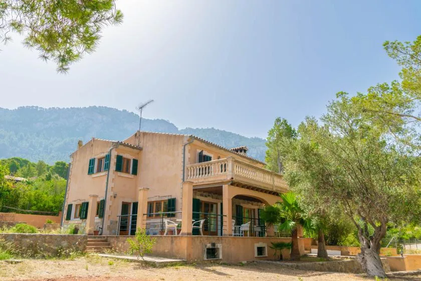 A peach-colored house with a covered terrace stands among trees beneath a mountain ridge.