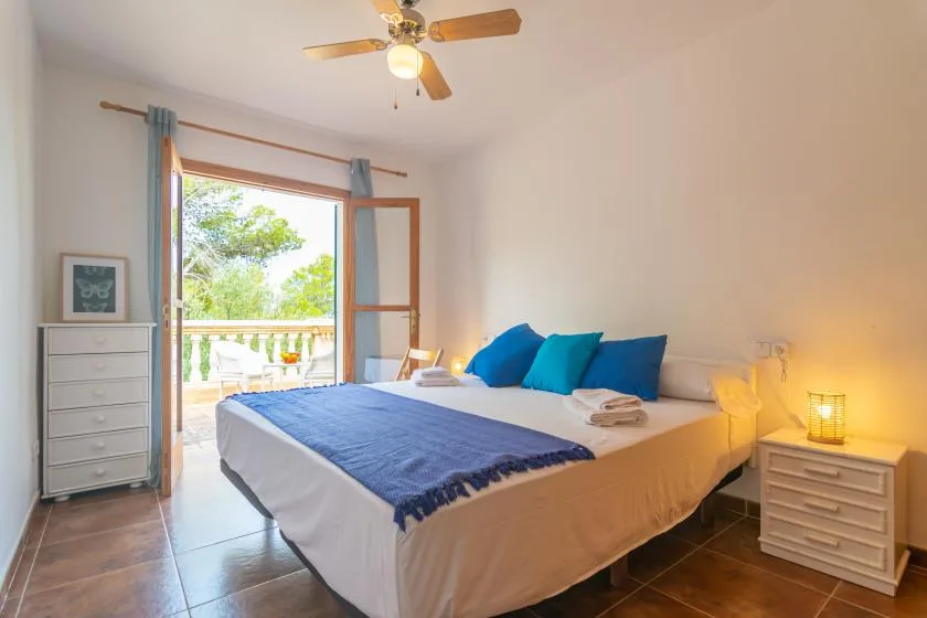 A bright bedroom with a neatly made bed and an open balcony door.
