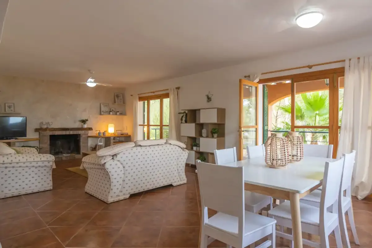A living and dining area with seating, a fireplace, and a table by open windows.