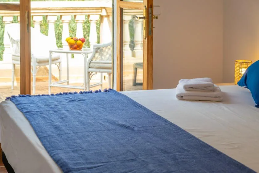 A bedroom with a bed and folded towels, opening onto a sunlit balcony.