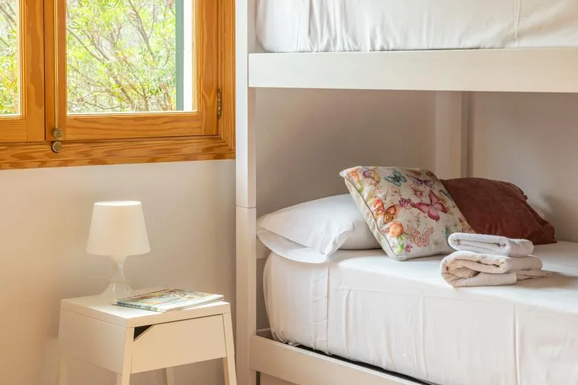 A bedroom with a bunk bed, pillows, and a wooden-framed window.