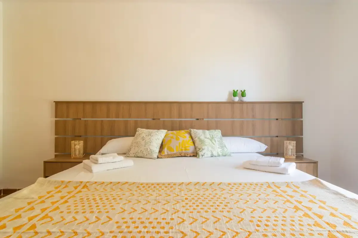 A bedroom with a neatly made bed and patterned yellow bedding.