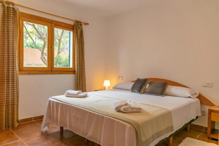A bedroom with a neatly made bed and a window overlooking greenery.