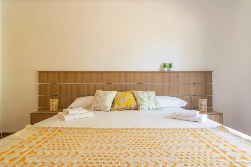 A bedroom with a neatly made bed and patterned yellow bedding.
