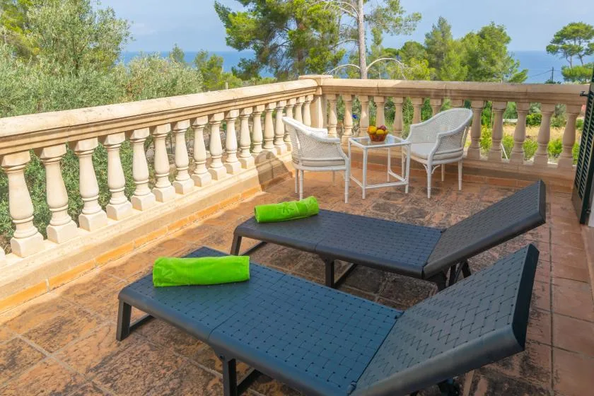A sunny terrace with dark reclining loungers and a small table by the balustrade.